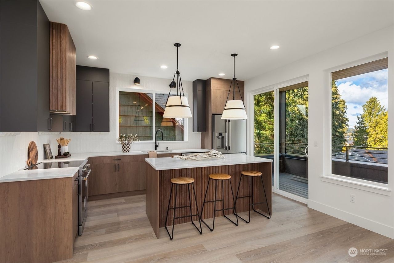 A kitchen with a large island and stools and a sliding glass door.