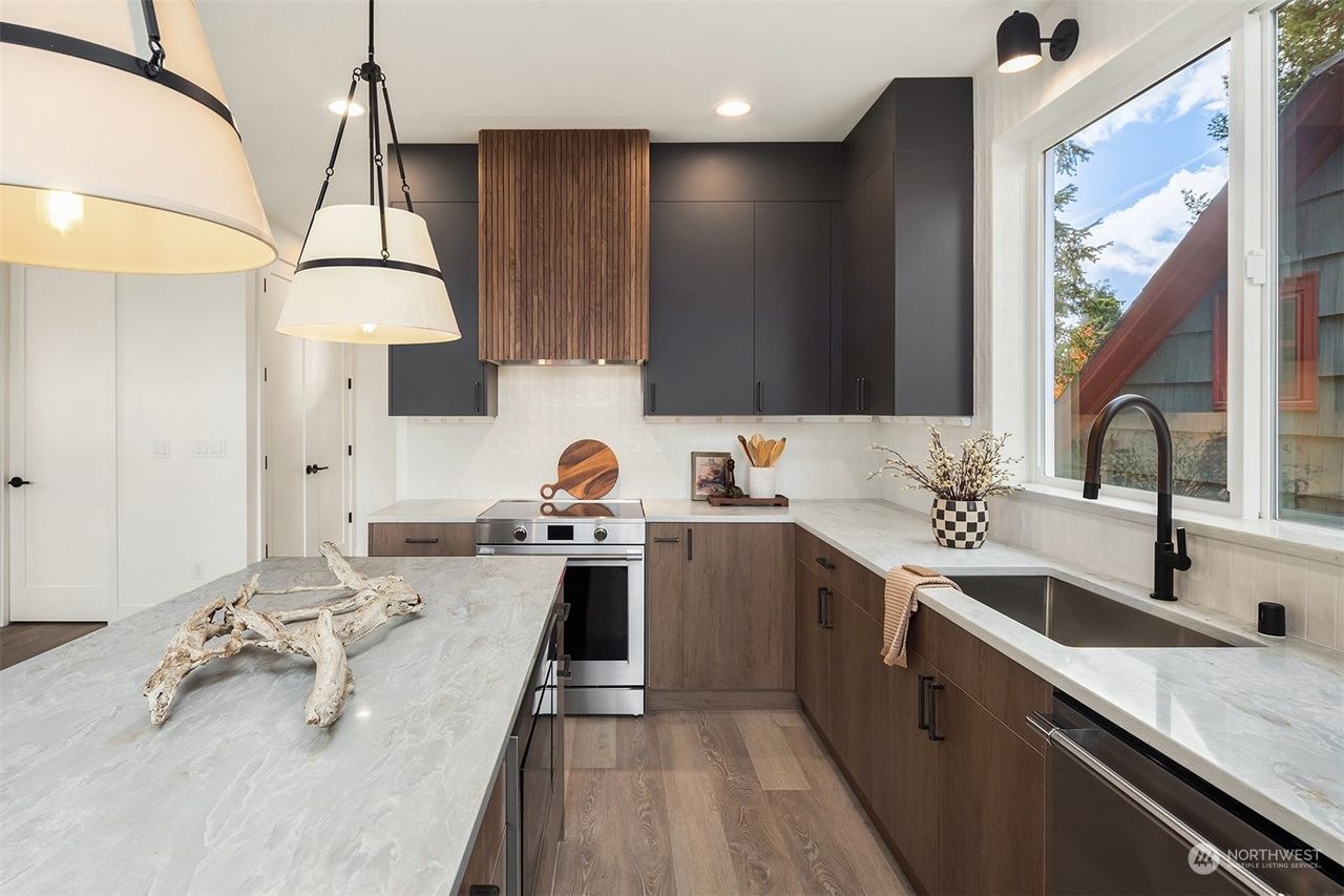 A kitchen with stainless steel appliances , wooden cabinets , a sink , and a large window.