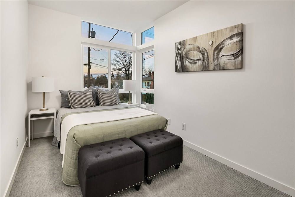 A bedroom with a bed , two ottomans and a painting on the wall.