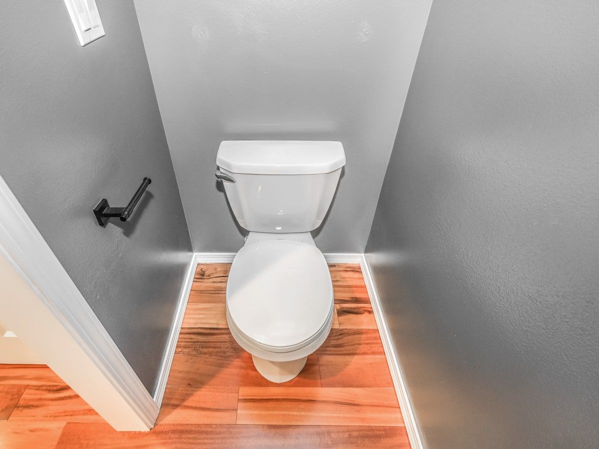 A toilet is sitting in a small bathroom with a wooden floor.