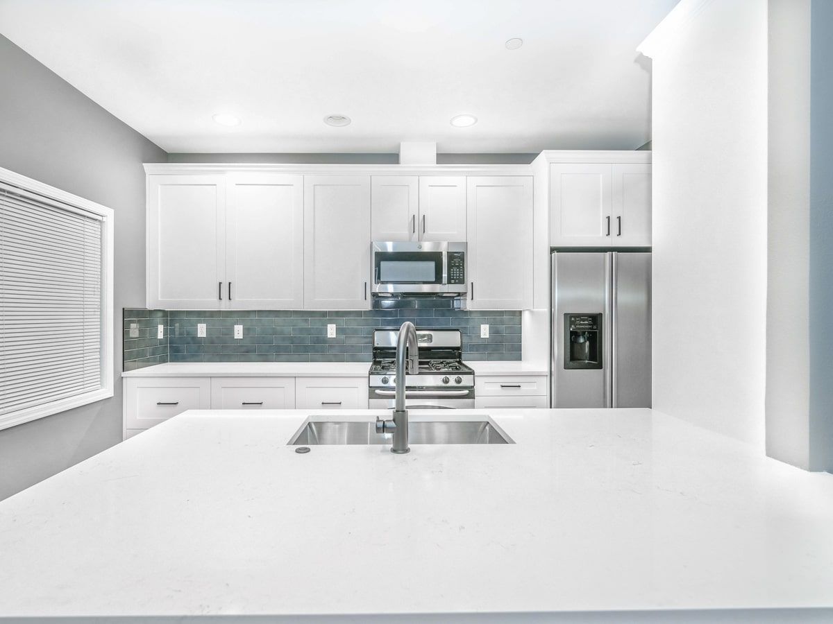 A kitchen with white cabinets , stainless steel appliances , a sink and a refrigerator.