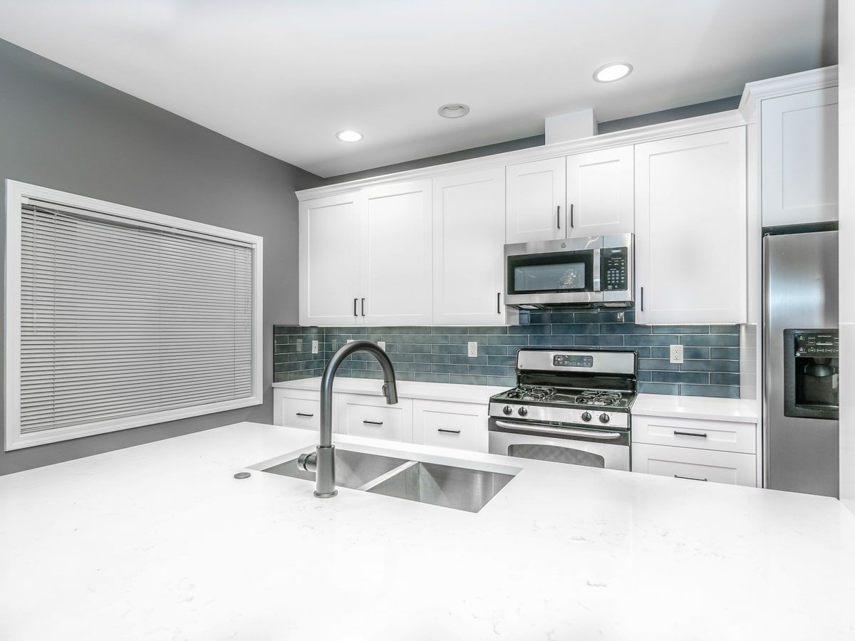A kitchen with white cabinets , stainless steel appliances , a sink and a refrigerator.