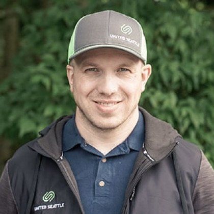 A man wearing a baseball cap and a jacket is smiling for the camera.