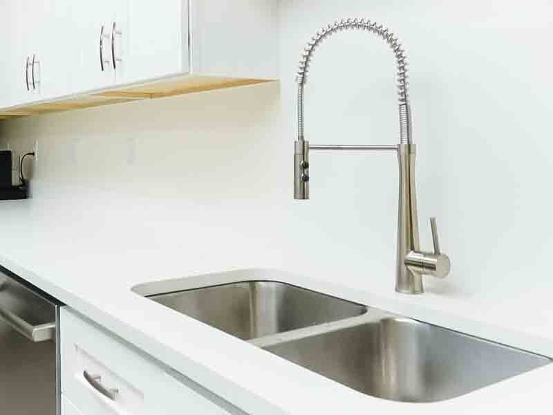 A kitchen sink with a stainless steel faucet and white counter tops.