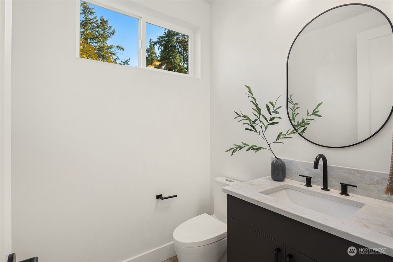 A bathroom with a toilet , sink , mirror and window.