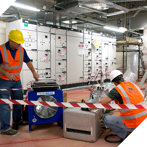 A man wearing a yellow hard hat is working on a fan