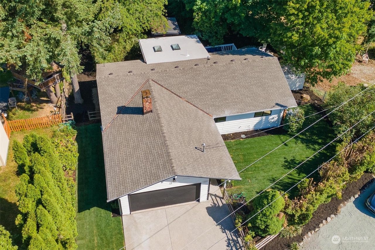 An aerial view of a house with a garage and a driveway surrounded by trees.
