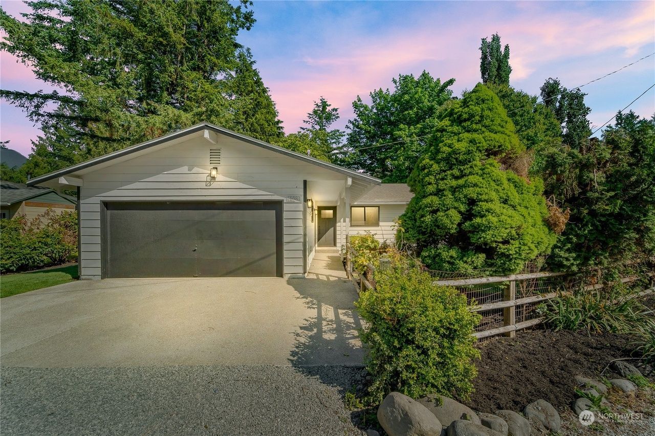 A white house with a black garage door is surrounded by trees.