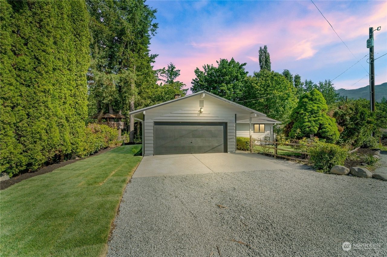 A garage with a driveway leading to it and a house in the background.