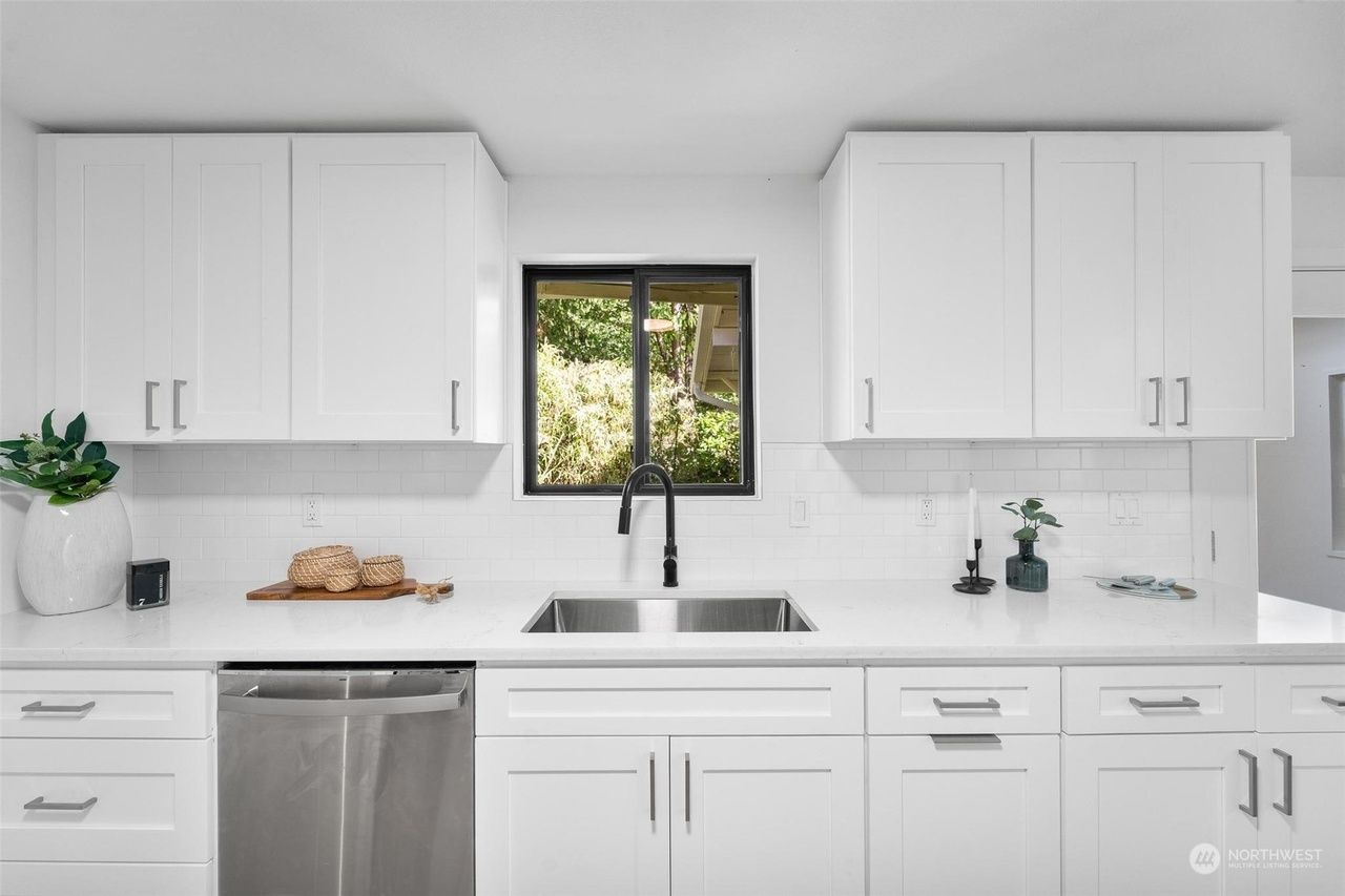A kitchen with white cabinets , a sink , a dishwasher and a window.