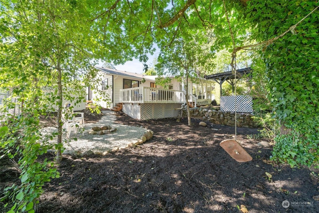 A house with a porch and a swing in the backyard surrounded by trees.