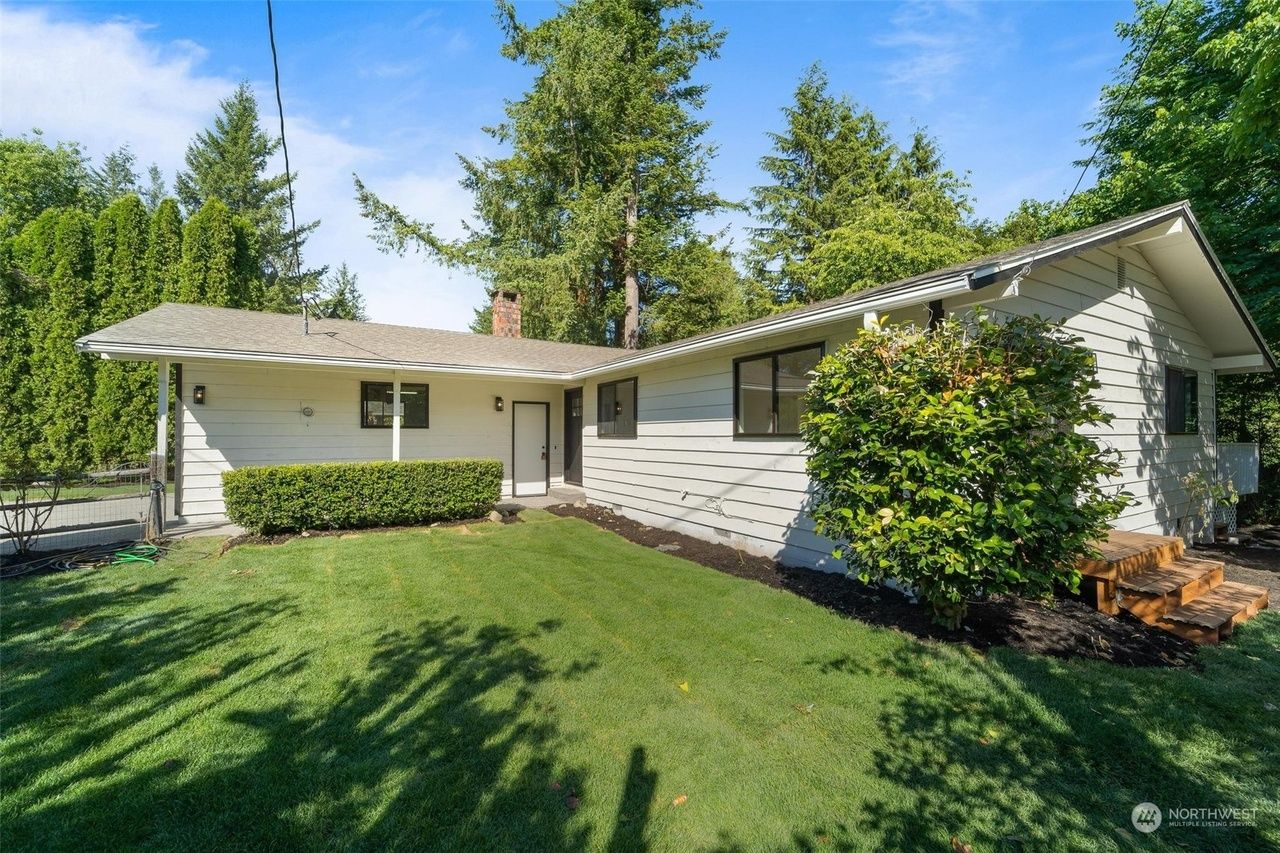 A white house with a large lawn in front of it surrounded by trees.
