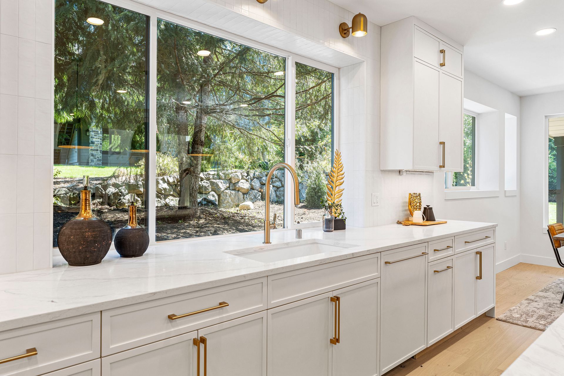 A kitchen with white cabinets , a sink , and a large window.
