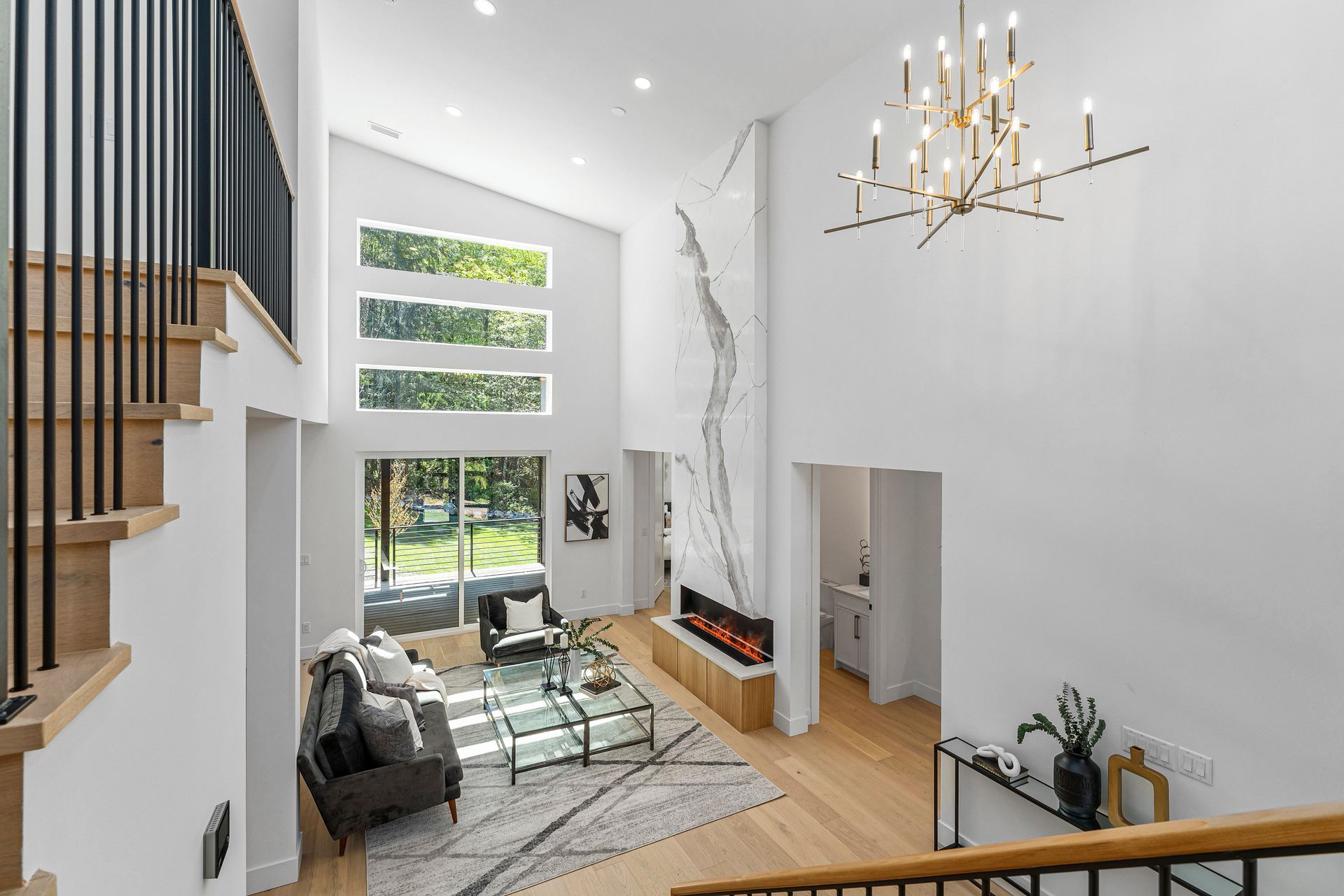 A living room with a couch , chairs , stairs and a chandelier.