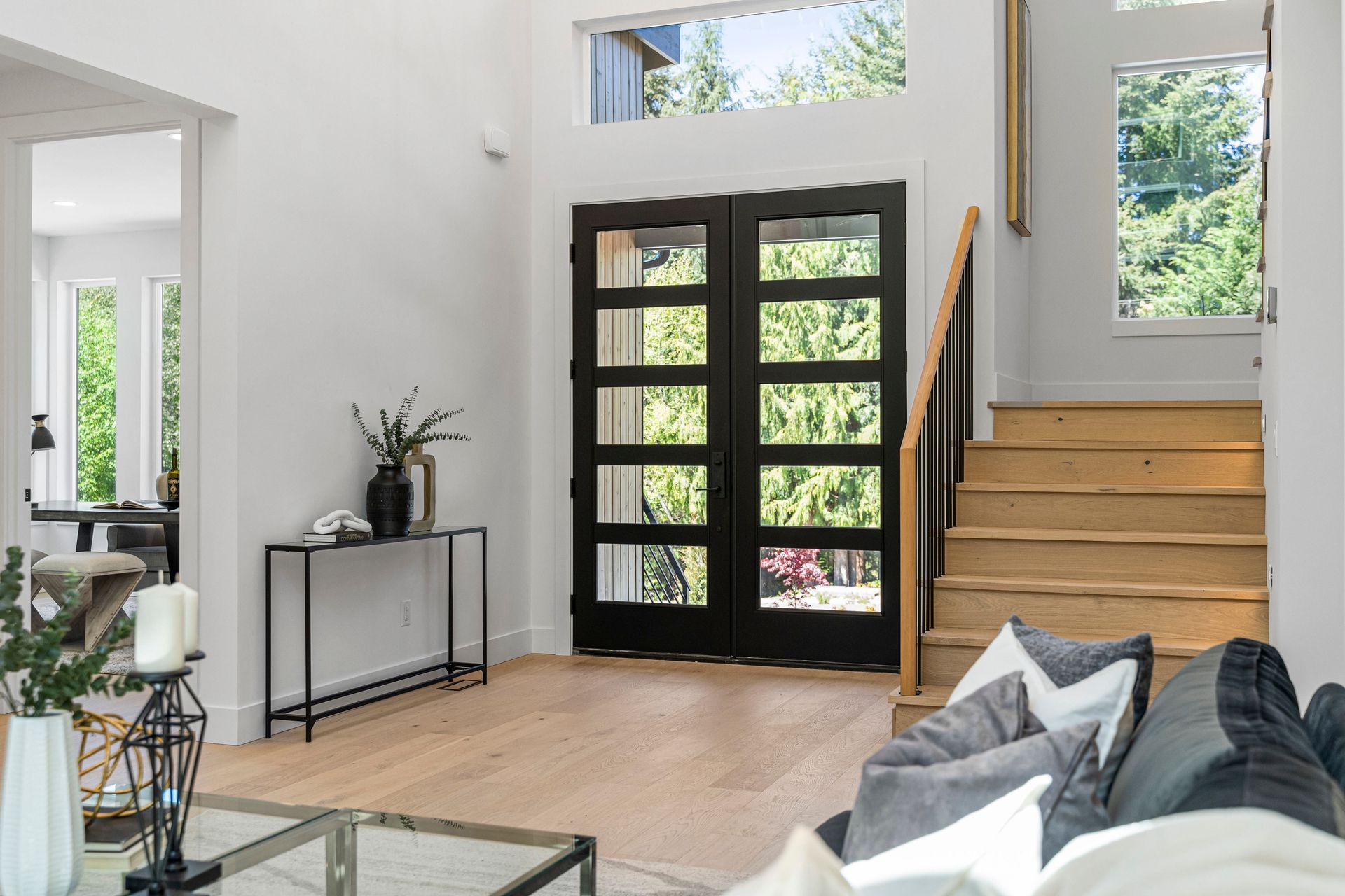 A living room with a couch , table , stairs and a black door.