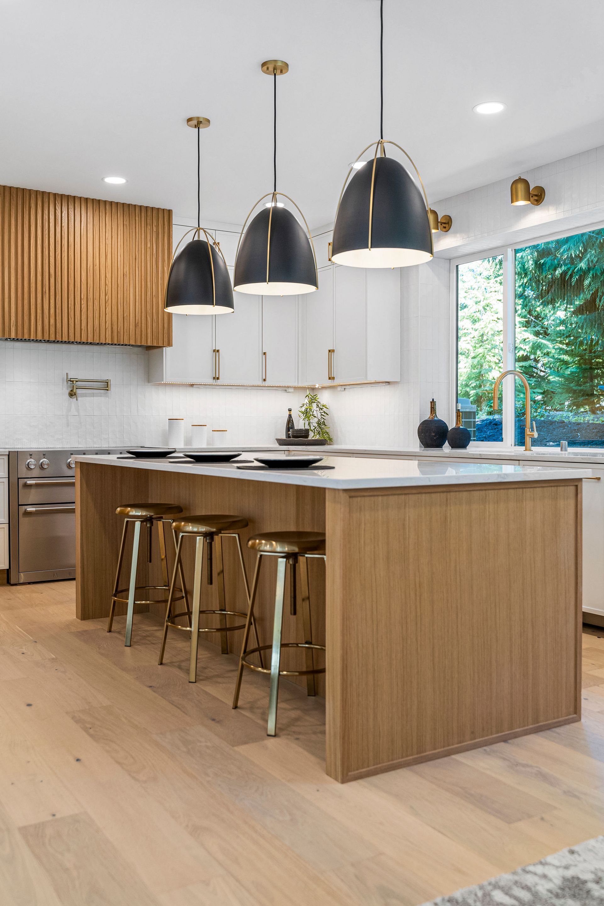 A kitchen with a large island , stools and pendant lights.