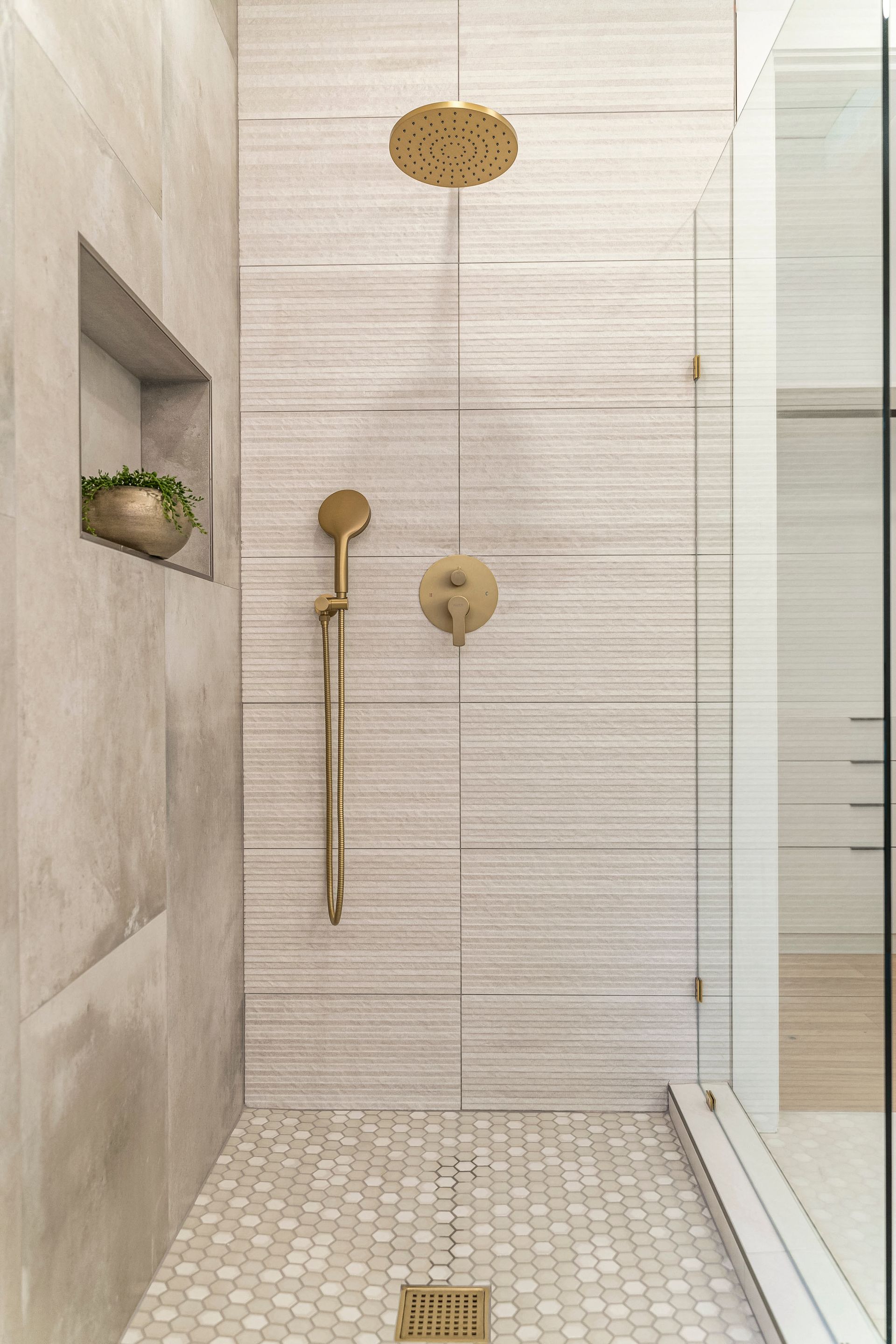 A bathroom with a walk in shower with a gold shower head.