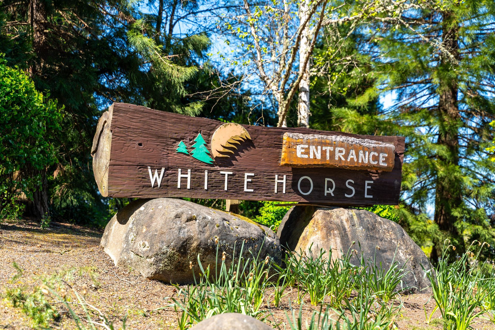 A wooden sign for white horse entrance is sitting on top of a rock.