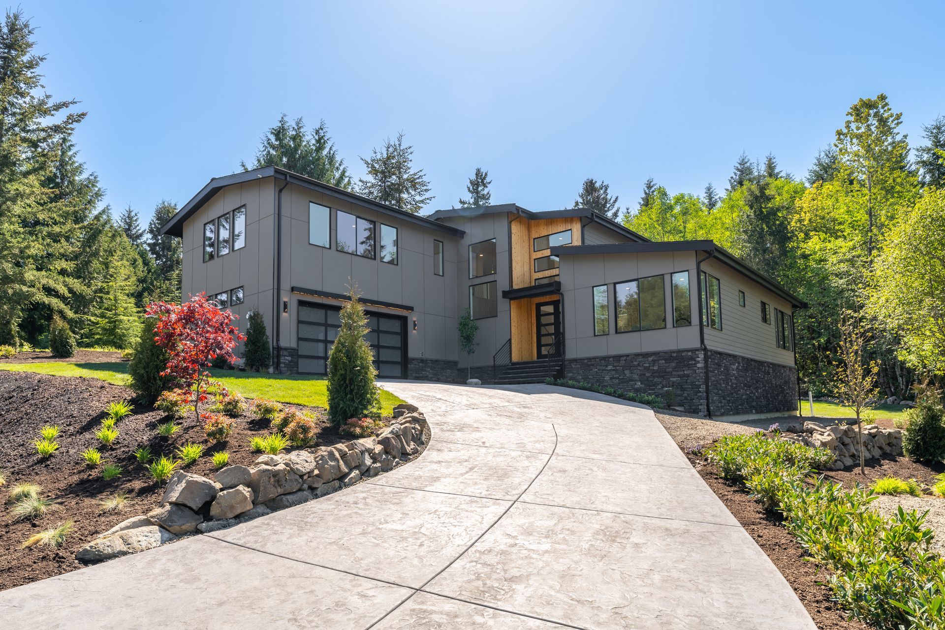A large house with a concrete driveway leading to it is surrounded by trees.