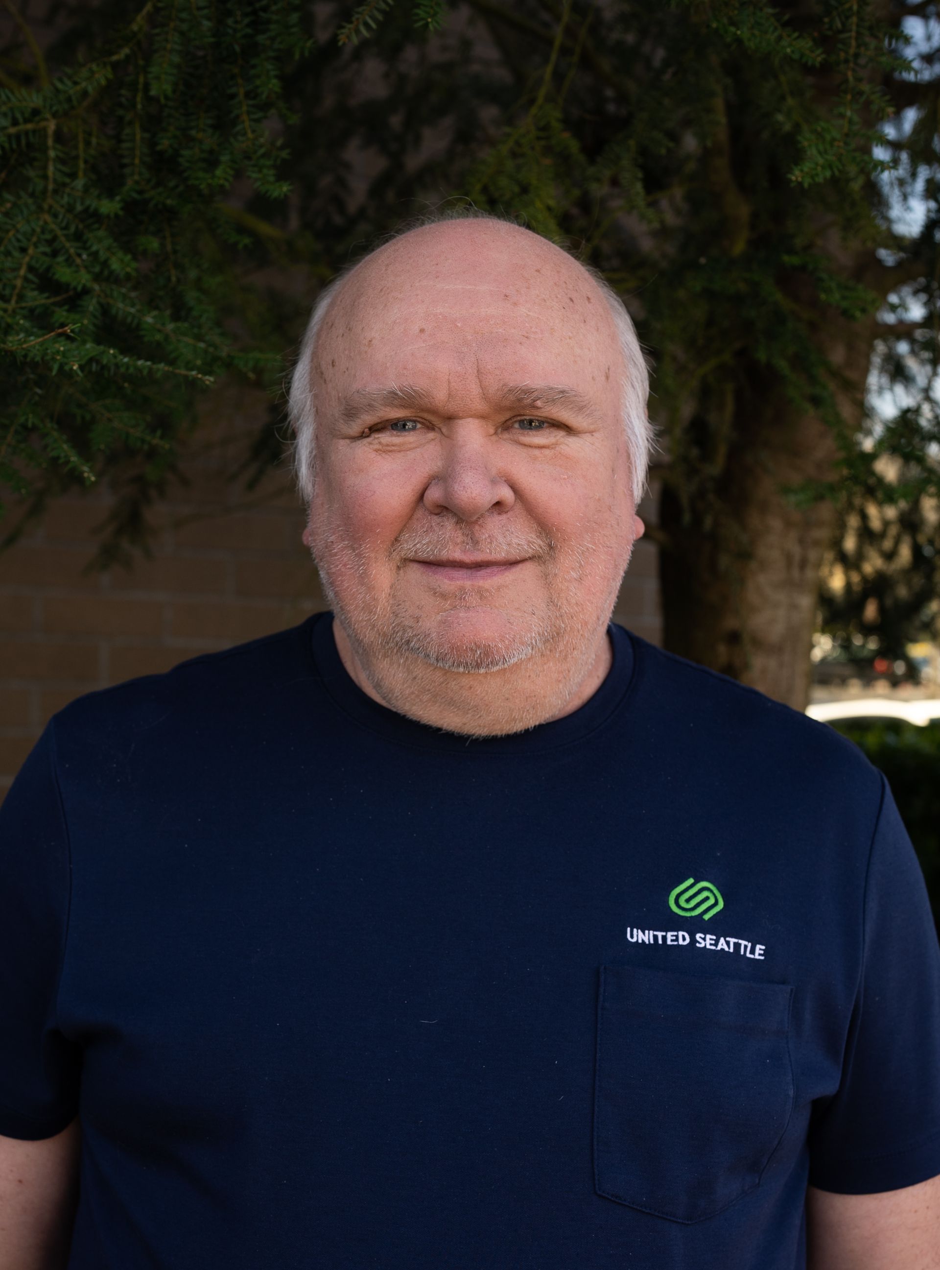 A man in a blue shirt is standing in front of a tree.