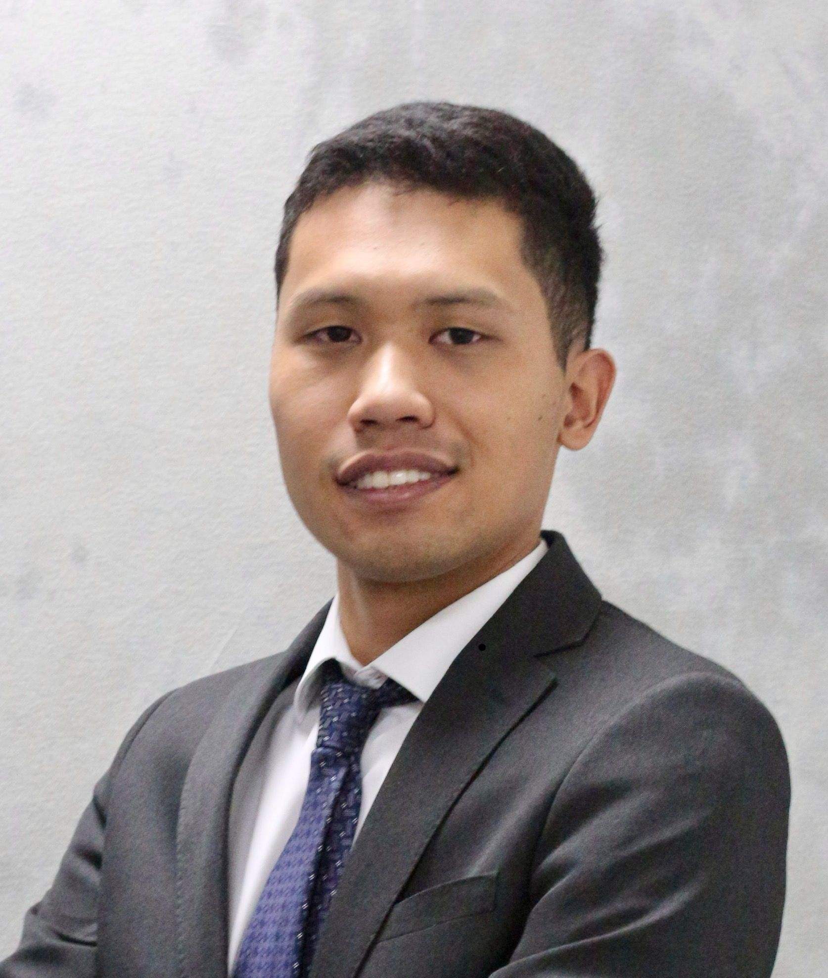 A young man wearing a black t-shirt is standing in front of a tree.