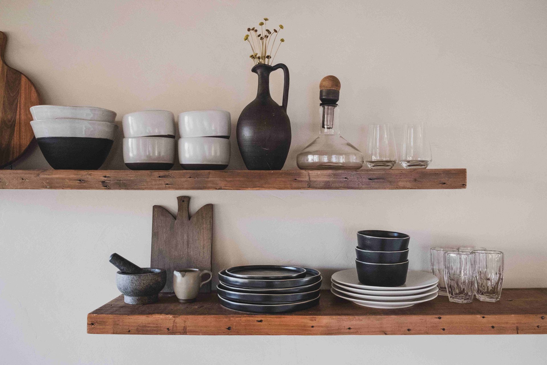 A wooden shelf with plates , bowls , glasses and a vase on it.