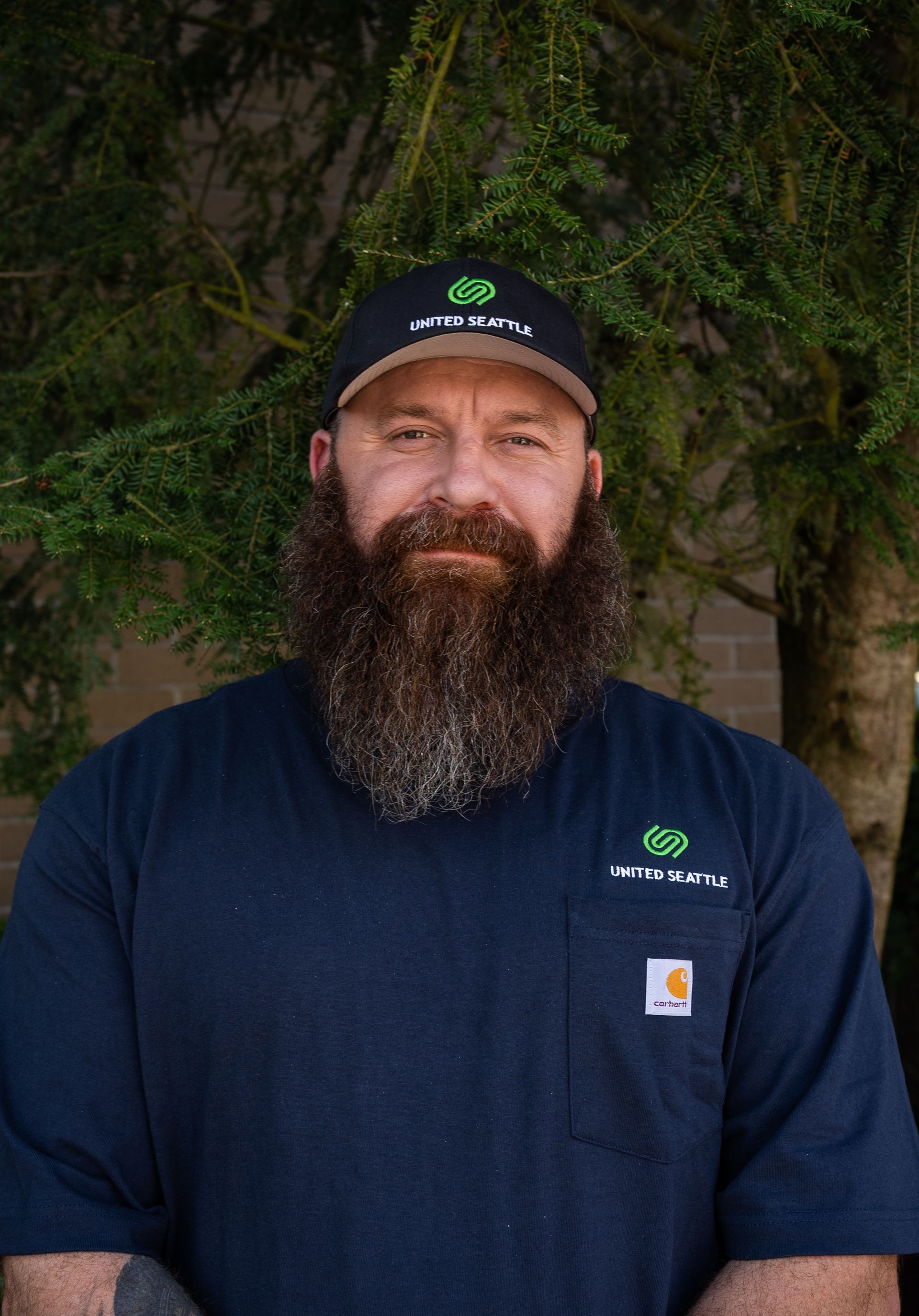 A man with a beard is wearing a hat and a blue shirt.