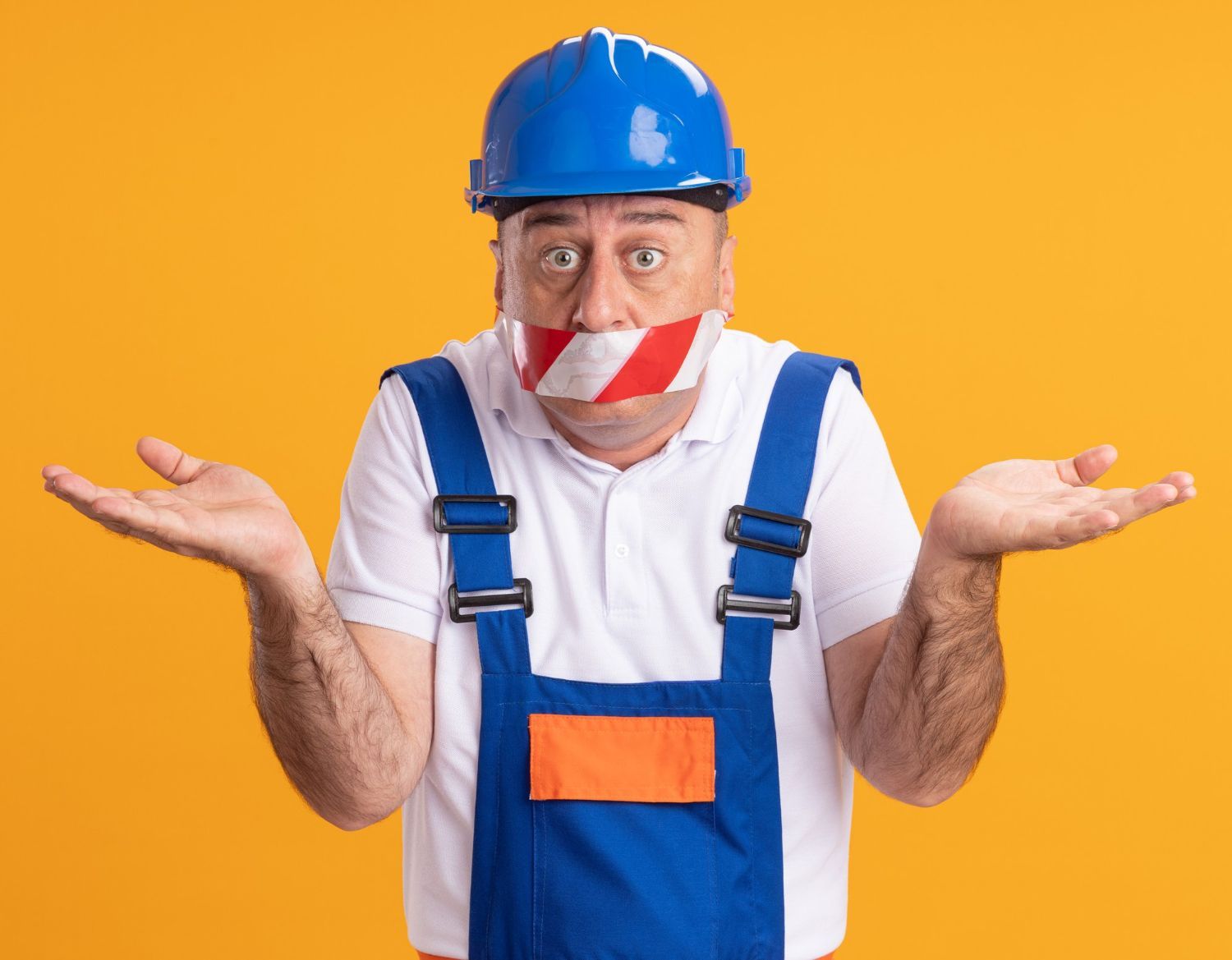 A man wearing a hard hat and overalls has tape on his mouth.