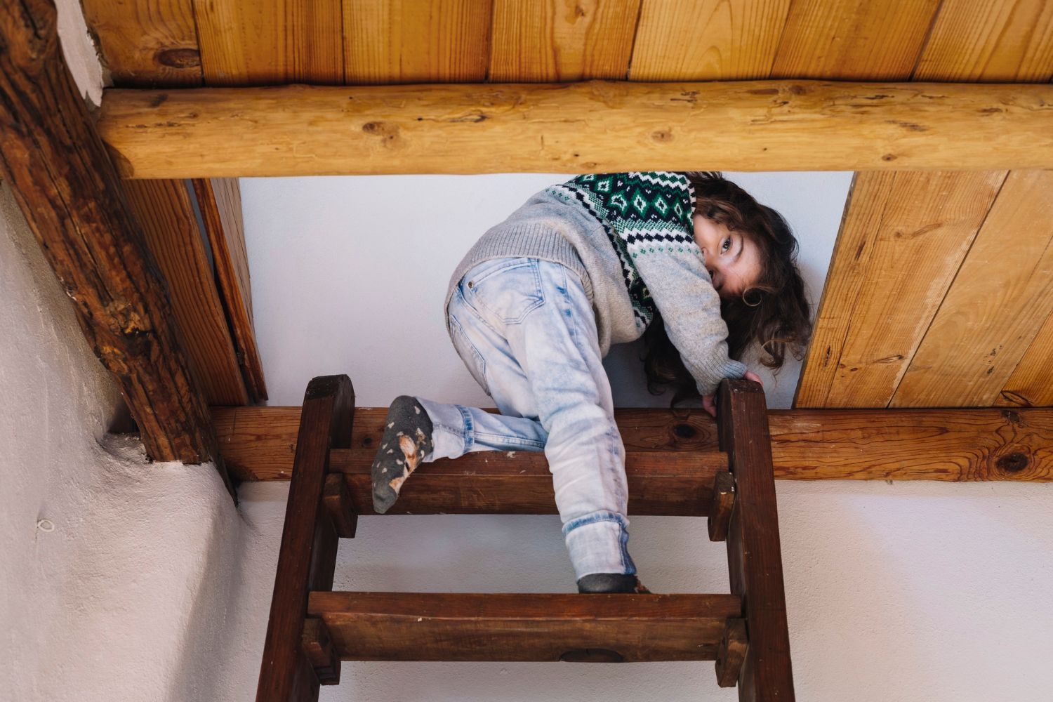 A little girl is climbing up a wooden ladder.