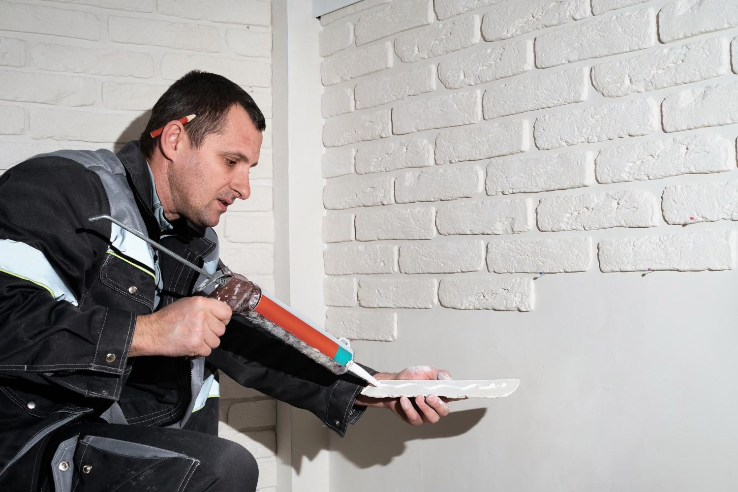 A man is gluing a tile to a white brick wall.