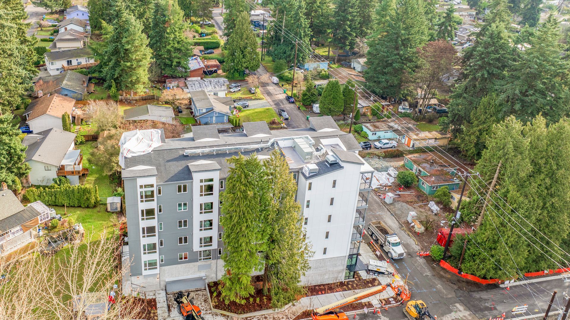 An aerial view of a building under construction in a residential area surrounded by trees.