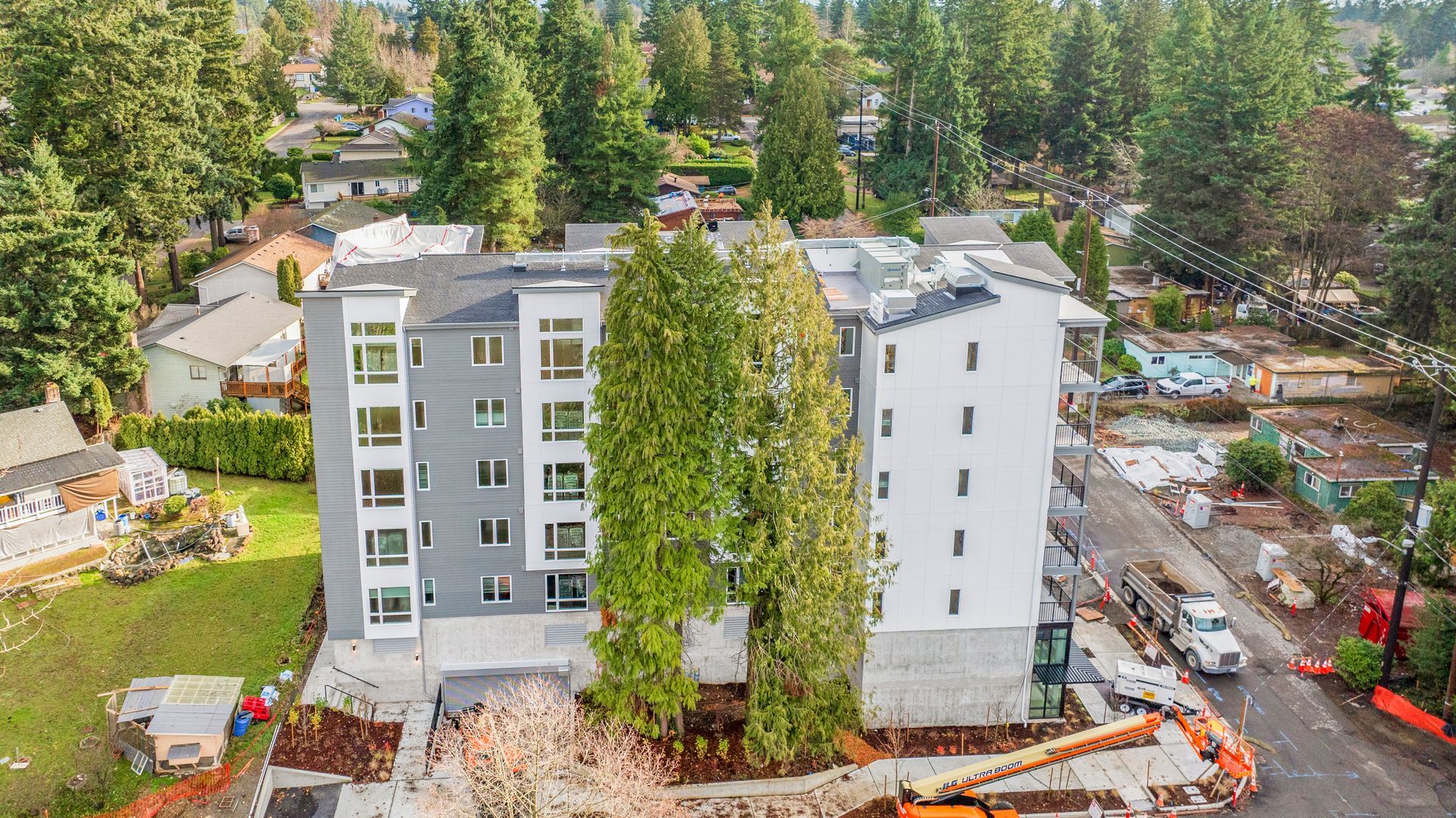 An aerial view of a building under construction in a residential area surrounded by trees.