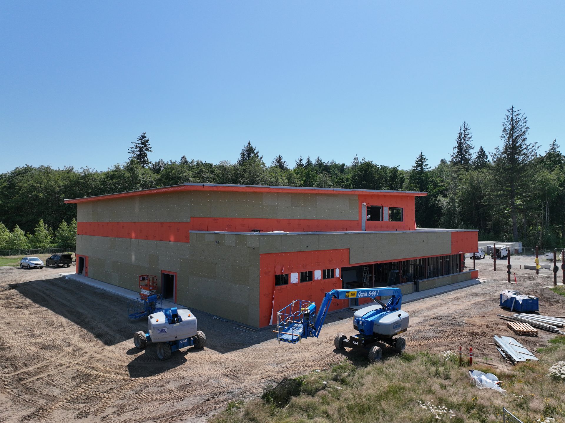 A large building is being built in a field with trees in the background.