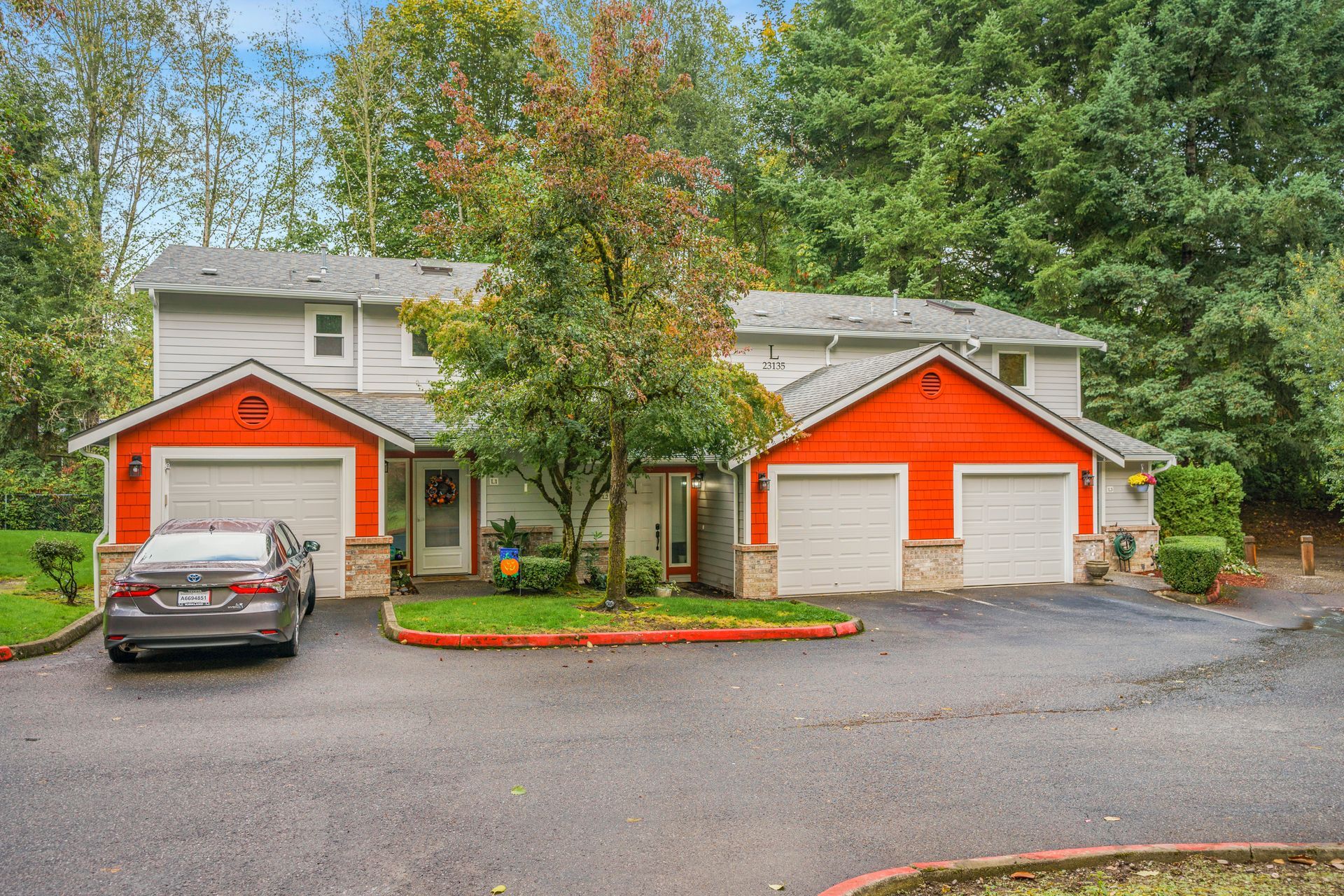 A car is parked in front of a house with two garages.