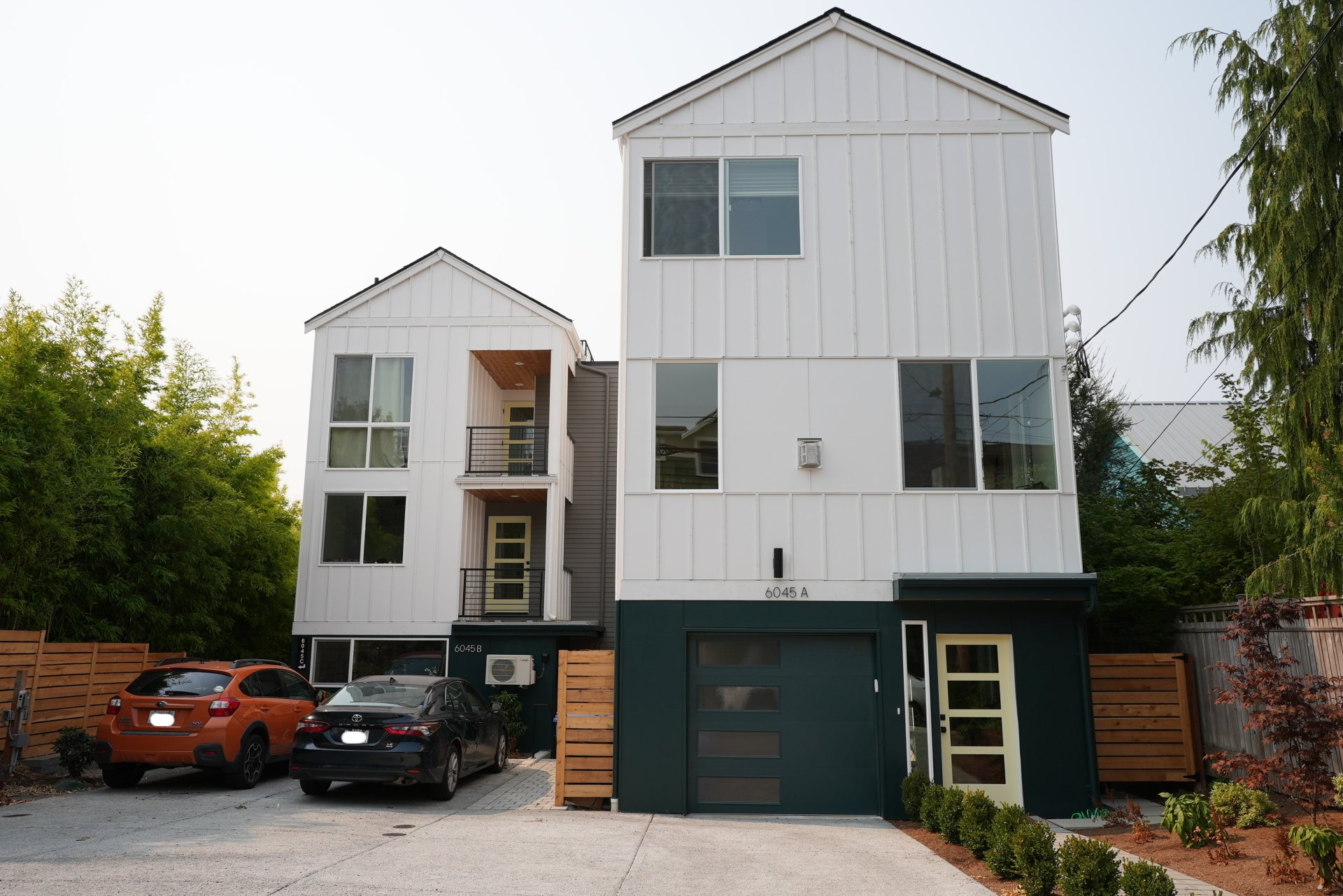 A white house with a green garage and two cars parked in front of it.
