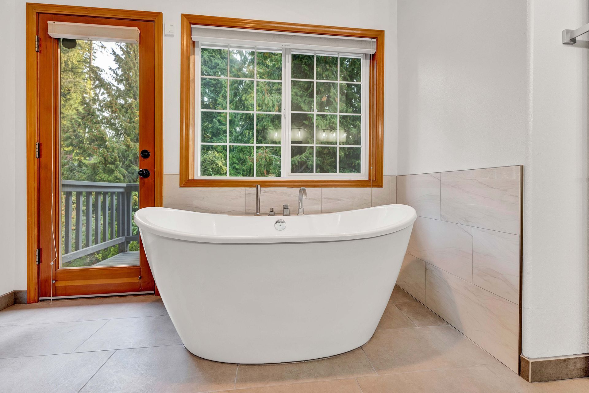 A bathtub in a bathroom next to a window and a door.