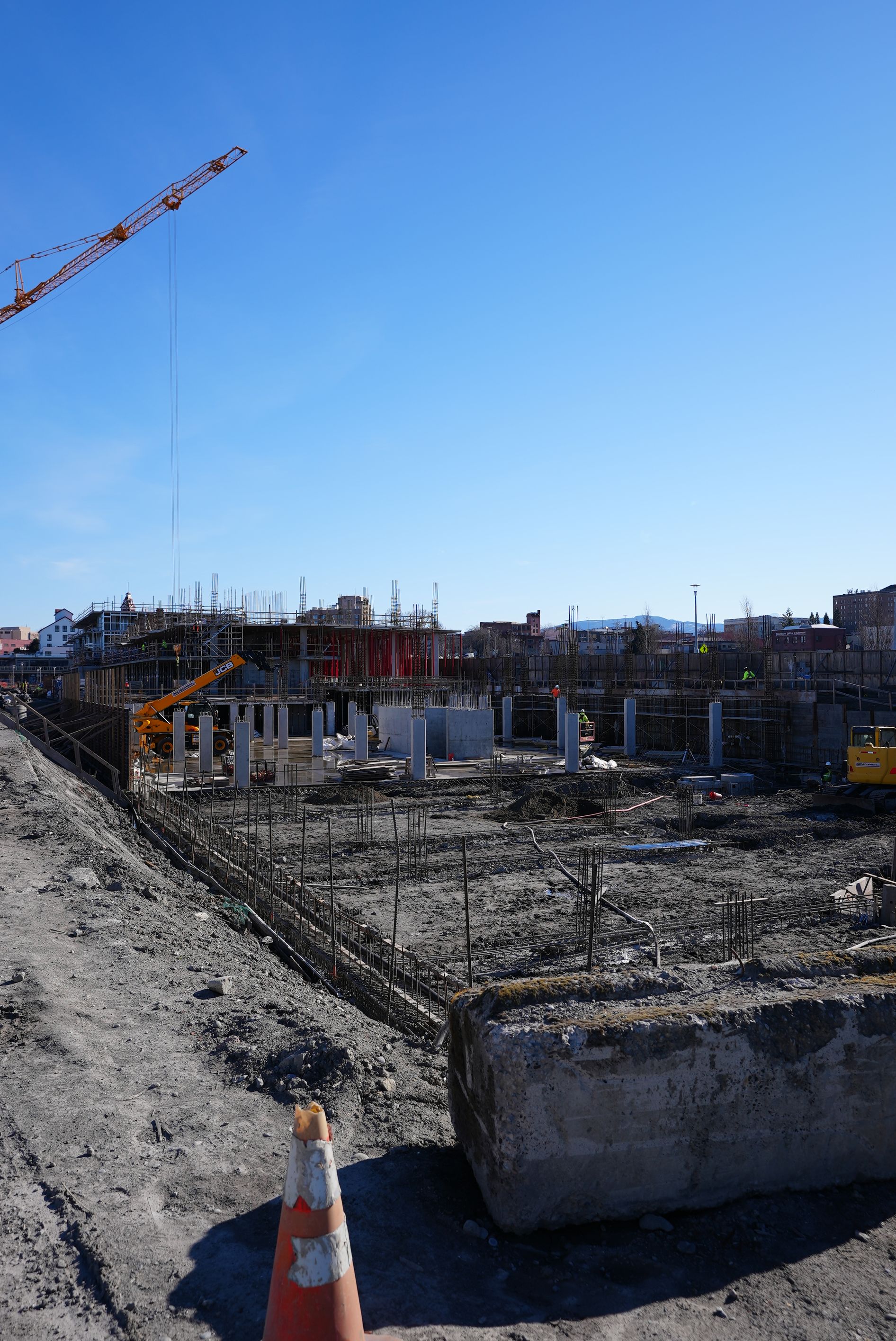 A construction site with a crane in the background and a cone in the foreground.