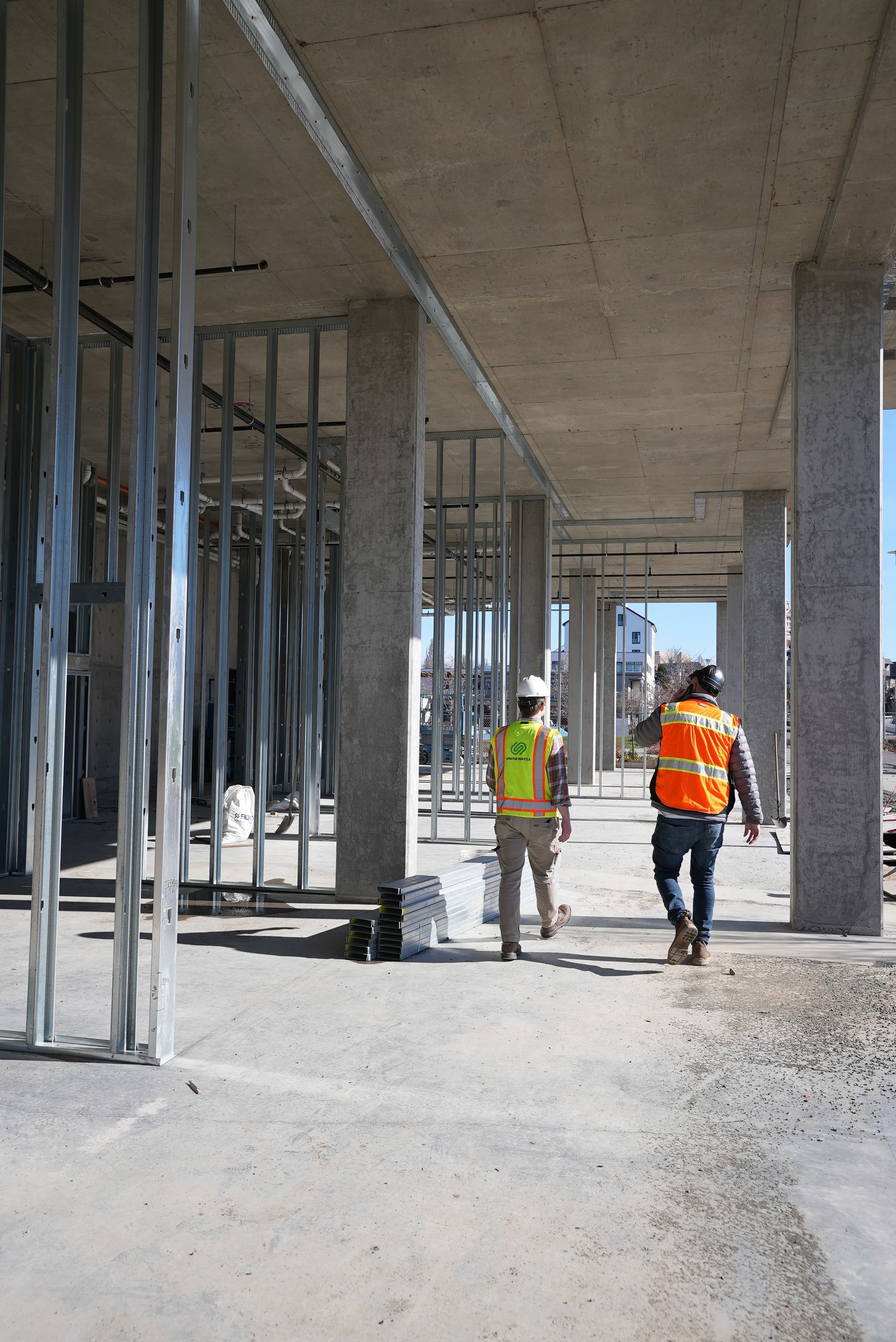 Two construction workers are walking through a building under construction.