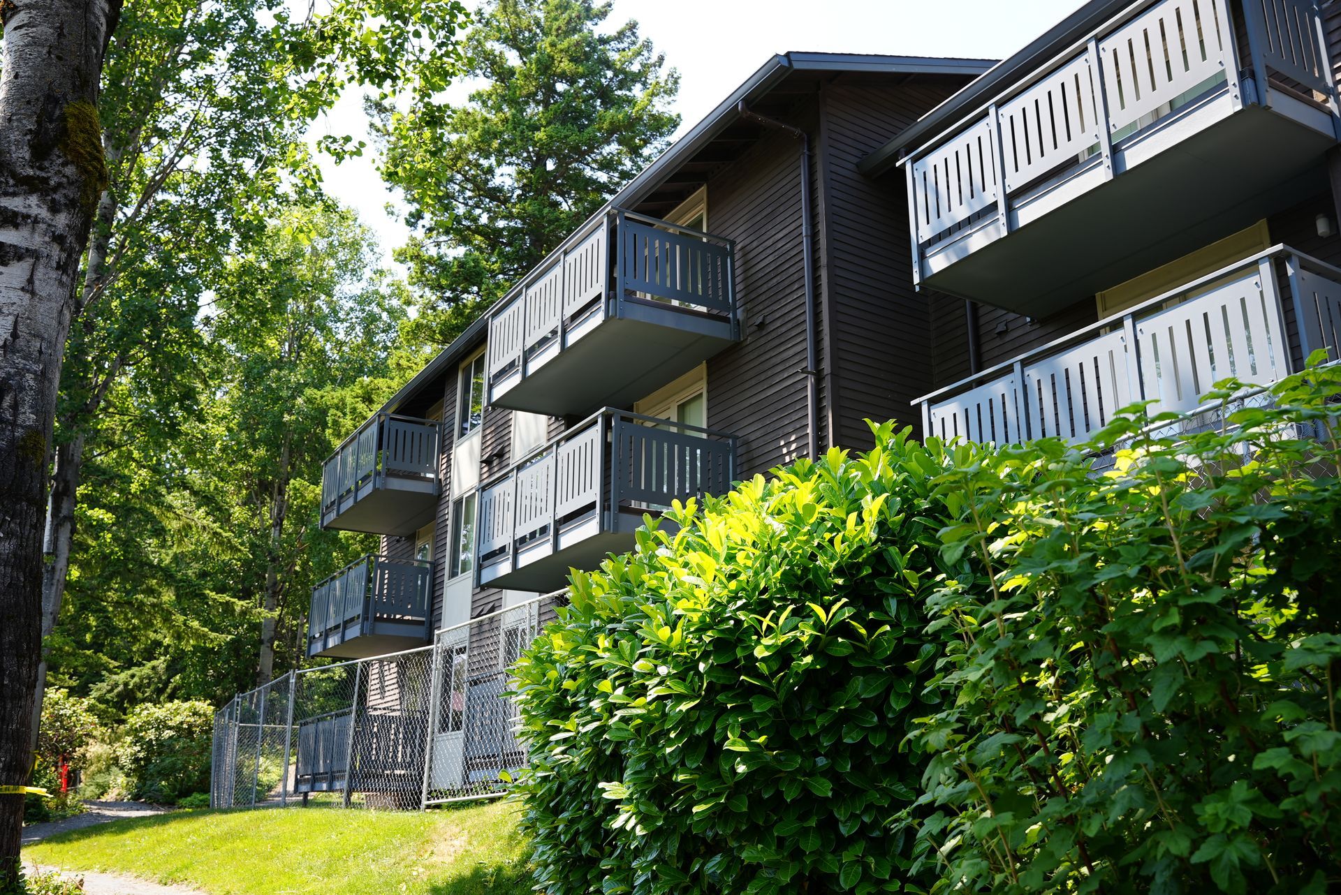 A large apartment building with balconies and bushes in front of it