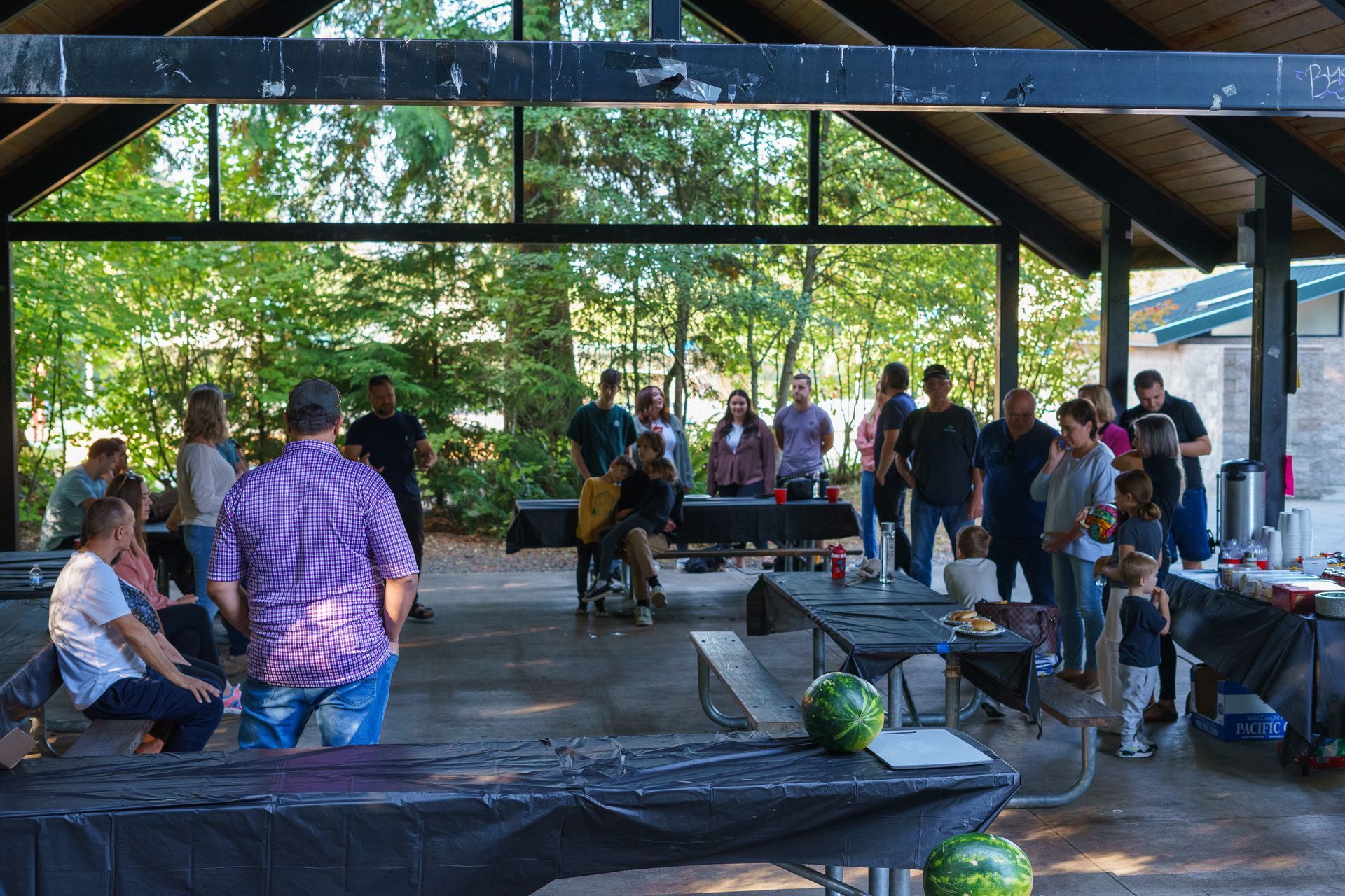 A group of people are standing around tables in a pavilion.