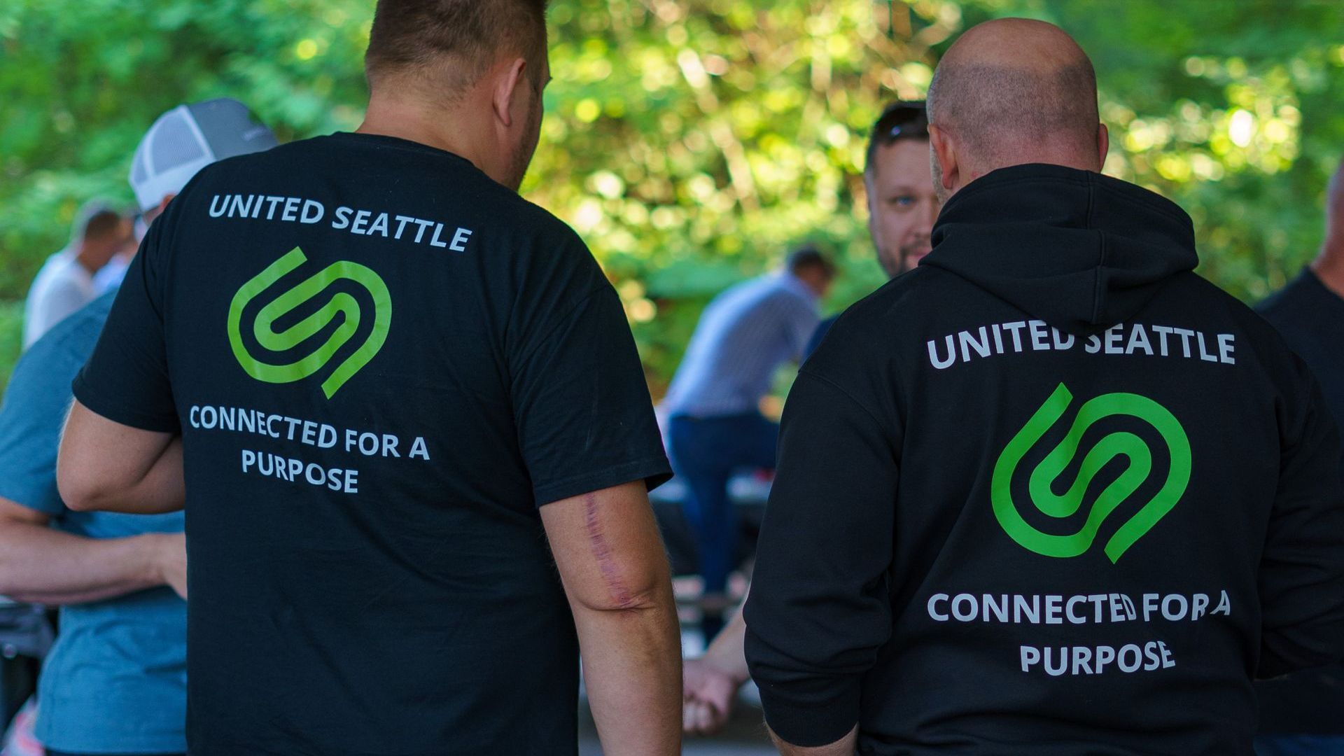 Two men are standing next to each other wearing united seattle shirts.