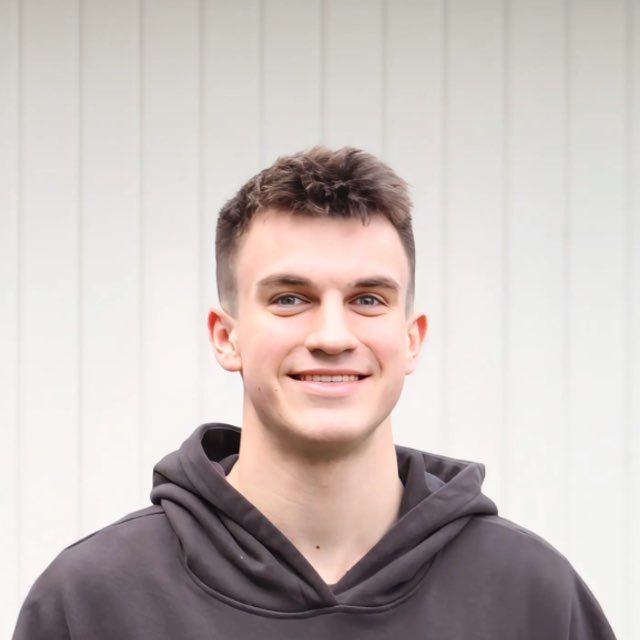 A man wearing glasses and a black shirt is standing in front of a tree.