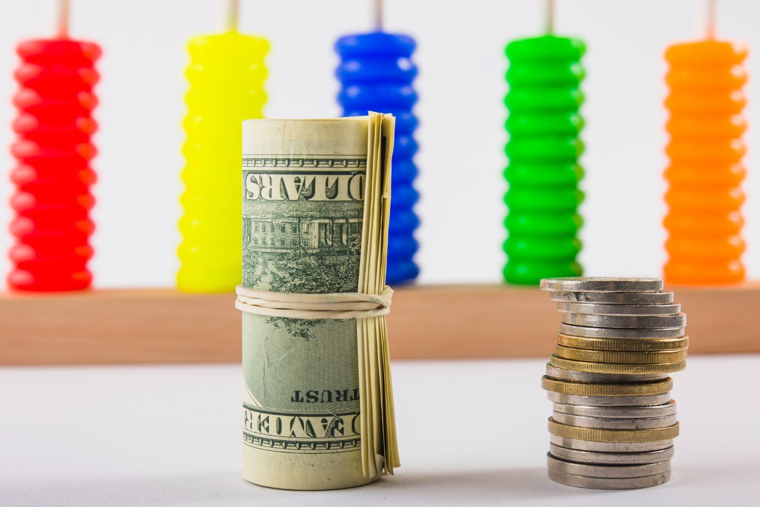 A roll of money next to a stack of coins and abacus in the background.