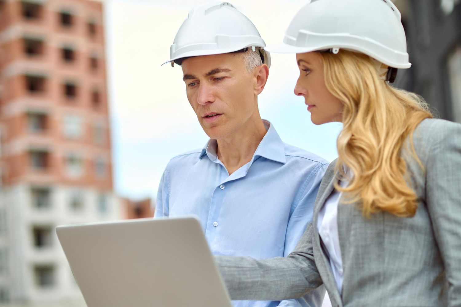 A man and a woman wearing hard hats are looking at a laptop.