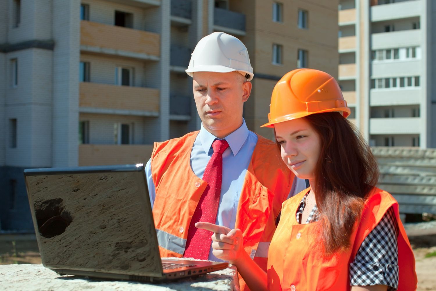 A man and a woman are looking at a laptop on a construction site.