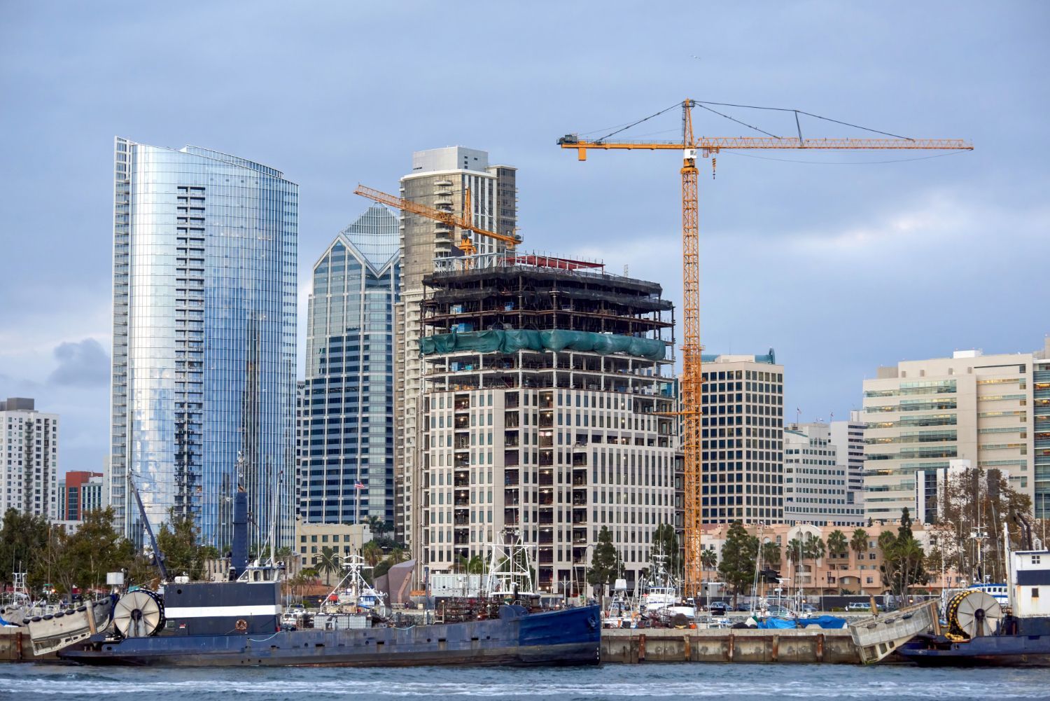 A city skyline with a crane in the foreground and a large building under construction in the background.