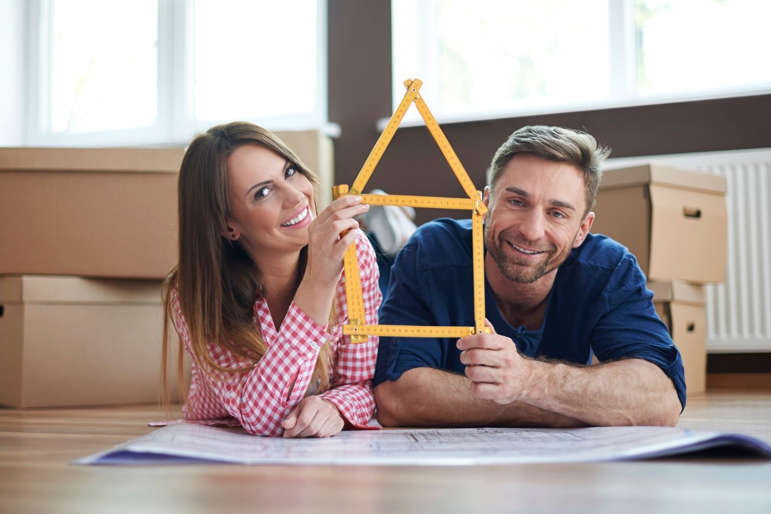 A man and a woman are laying on the floor holding a model of a house.