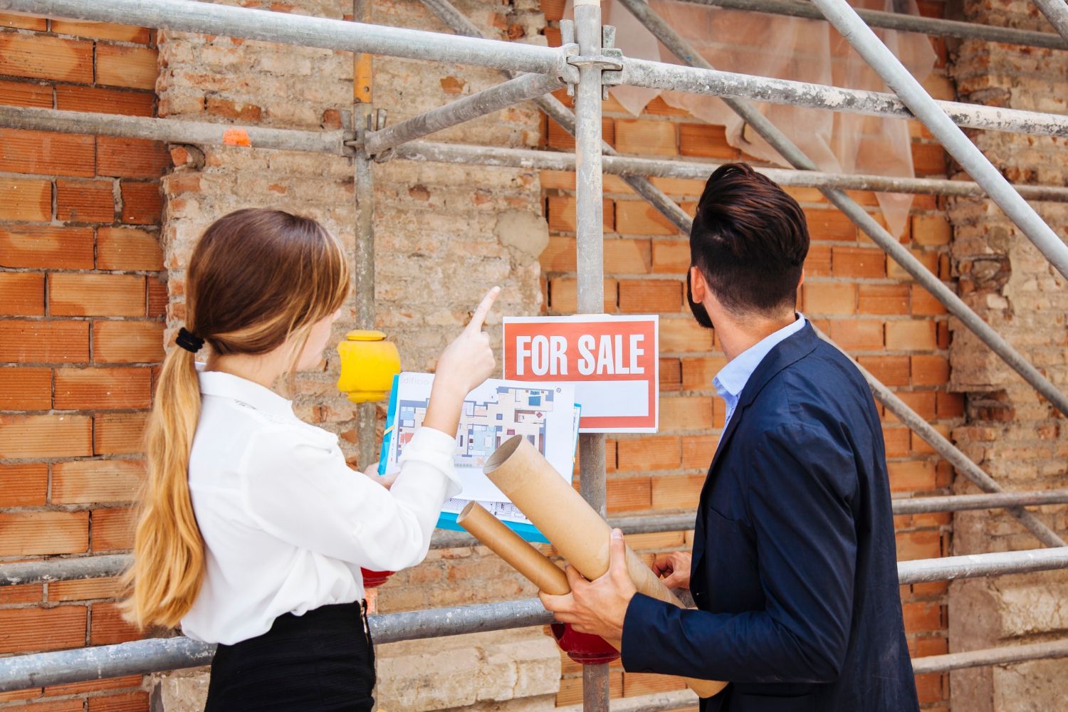 A man and a woman are standing next to a for sale sign.