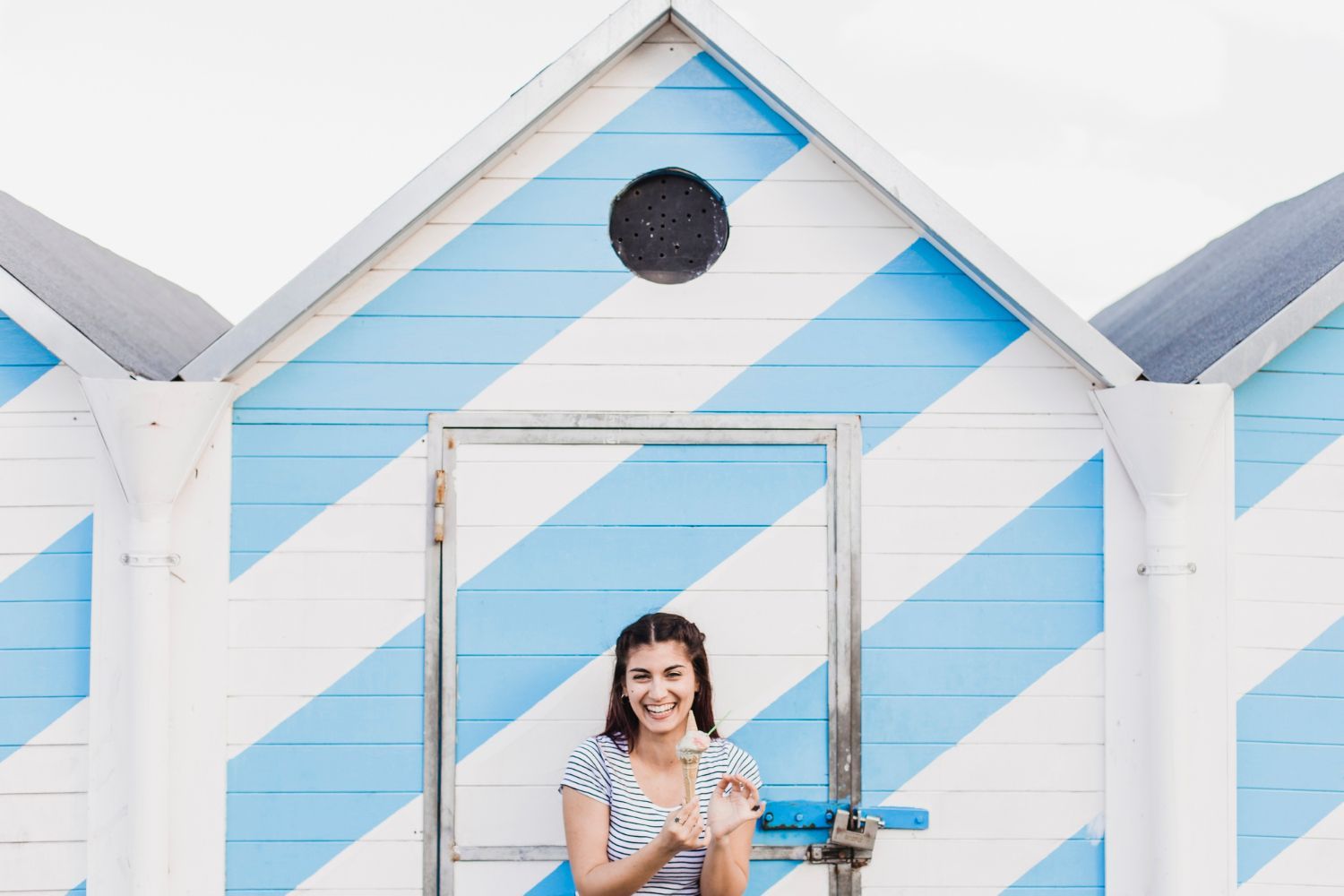 A woman is standing in front of a blue and white striped beach hut.