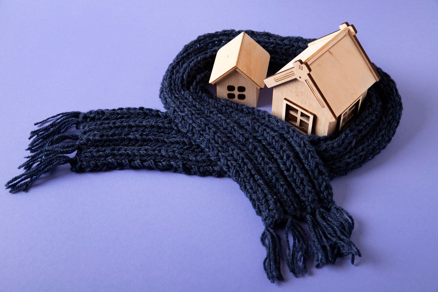 Two wooden houses are wrapped in a scarf on a purple background.